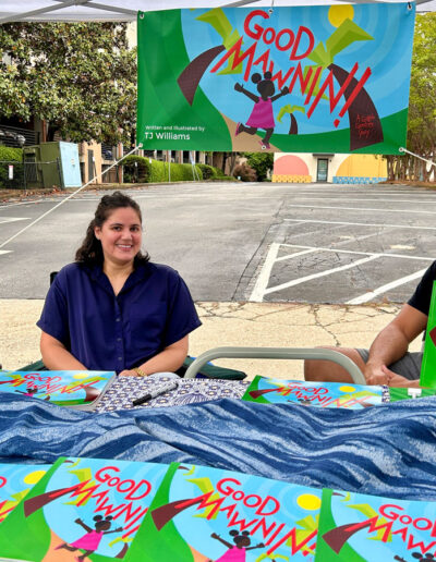 Two adults smiling at a booth promoting a book called “Good Mawnin!”