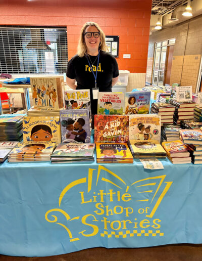 A Little Shop of Stories employee standing behind their booth with various books.