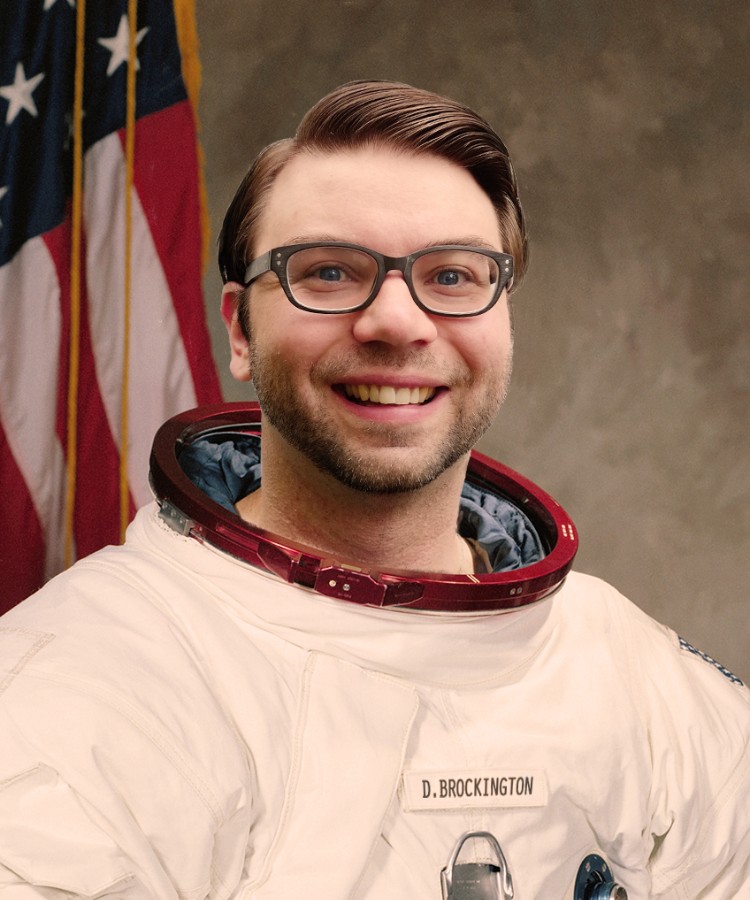 CatStronauts author Drew Brockington smiling in a professional NASA-style flight suit without a helmet.