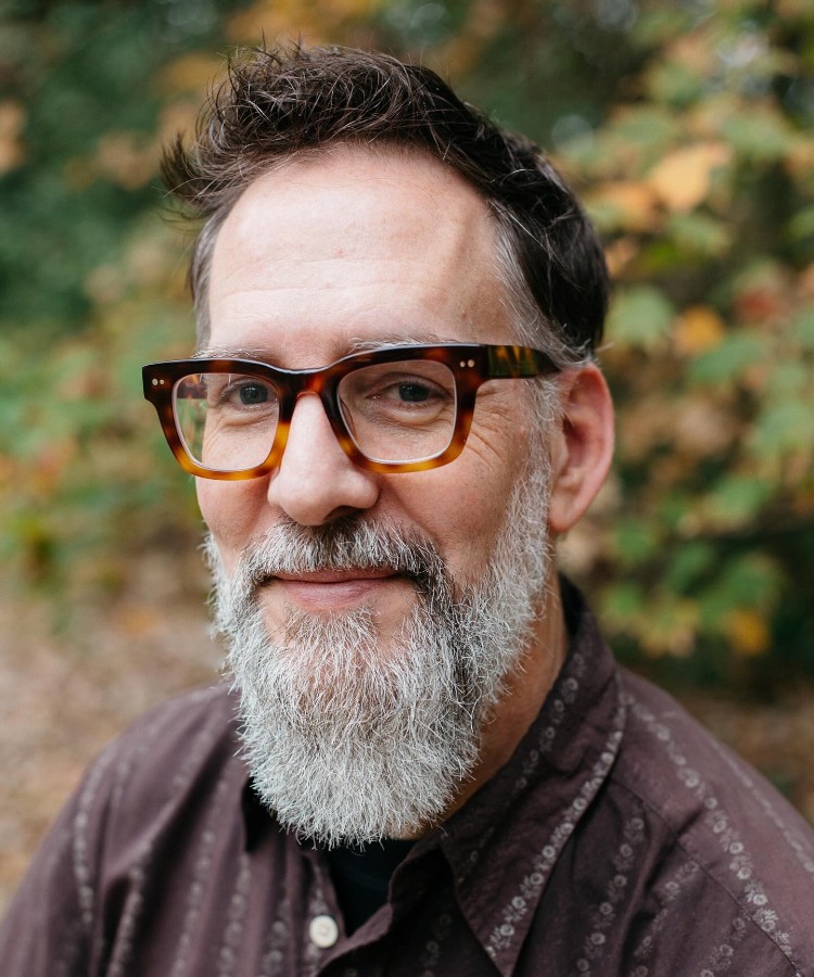 Headshot of artist Ward Jenkins looking directly at the camera with a smile. He has a full beard and is posed against a neutral background.